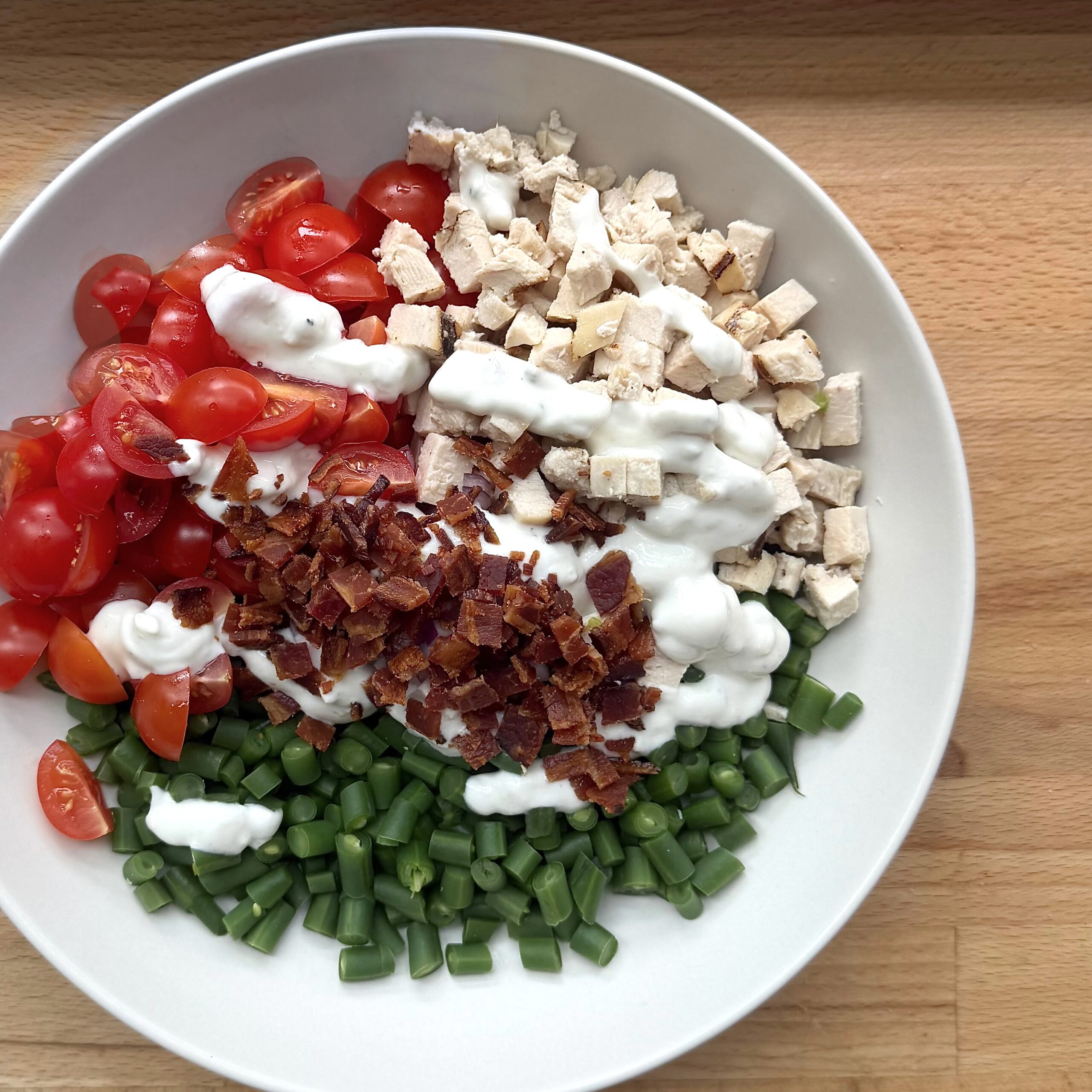 A chicken salad with green beans tomatoes and bacon. It is covered in a creamy blue cheese dressing